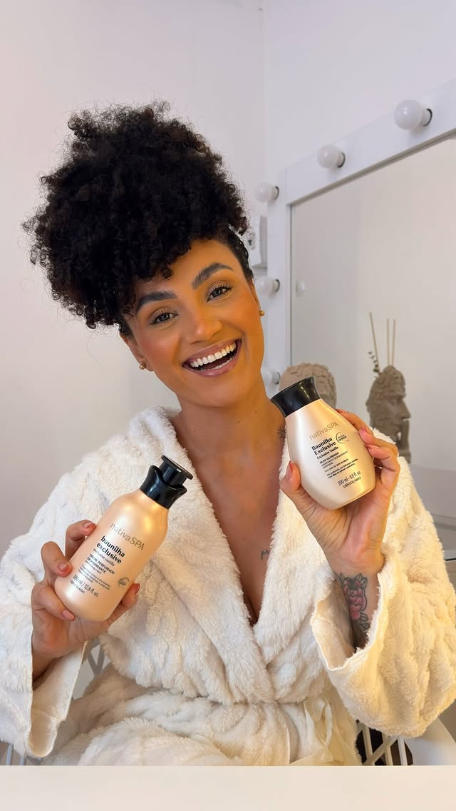 Nativa SPA Baunilha Exclusive une a intensidade da baunilha à hidratação profunda que sua pele merece. A @isabelasoulza_ entrou nesse ritual de autocuidado e veio mostrar toda a potência dessa combinação irresistível. 🤍✨São os últimos dias com até 20% de desconto desse lançamento com edição limitada. 😱Pele é assim, é Nativa SPA. #PeleNativaSPA #BaunilhaExclusive#OBoticário#PraGeralVer: A Isabela Souza, mulher negra, usa com cabelo cacheado preso para cima e um roupão na cor creme. Ao longo do vídeo ela mostra as embalagens da loção hidratante e do óleo e a textura de cada um na pele. by @oboticario